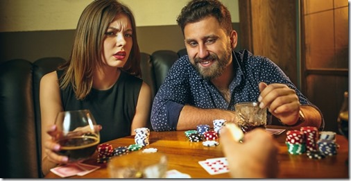 Male and female friends sitting at wooden table. Men and women playing card game. Hands with alcohol close-up. Poker, evening entertainment and excitement concept