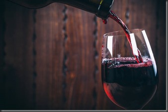 Pouring red wine into the glass against wooden background