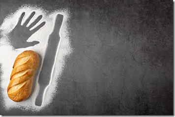 Baking dark background with fresh whole loaf of bread and outlines of ingredient flour of rolling pin and imprint of human hand top view with copy space