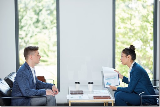 Serious young businesswoman showing financial report to emplyee and telling him off for poor figures