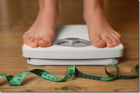 Overweight girl using scales near measuring tape on wooden floor, closeup