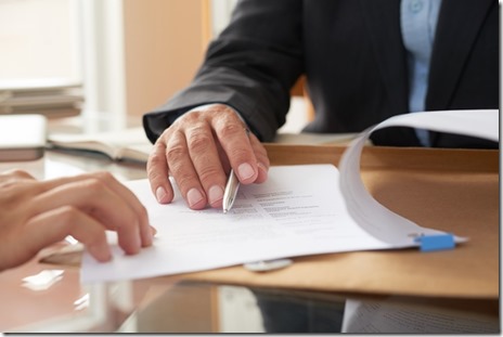 Close-up of businessman examining business contract and signing it at the office desk