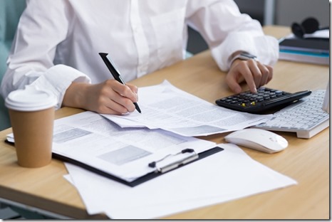 Close-up photo. Beautiful hands of a young woman in a white shirt. They write documents with a pen, calculate on a calculator at the table in the office, where there is a computer, a cup of coffee.