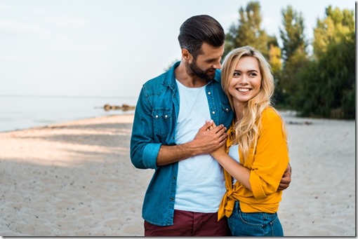 happy young couple hugging and walking on sandy beach