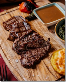 side view of grilled beef steak with sauce on a wooden board