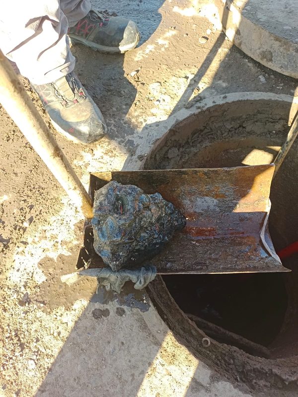 Personal técnico inspeccionando una cámara de alcantarillado obstruida por residuos de construcción