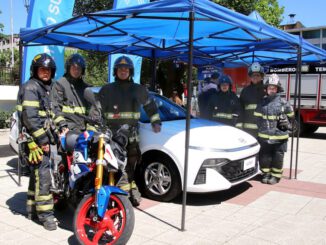 Voluntarios de Bomberos de Temuco presentando la Gran Rifa Monumental 2026 con un auto y moto en exhibición.