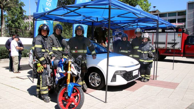 Voluntarios de Bomberos de Temuco presentando la Gran Rifa Monumental 2026 con un auto y moto en exhibición.